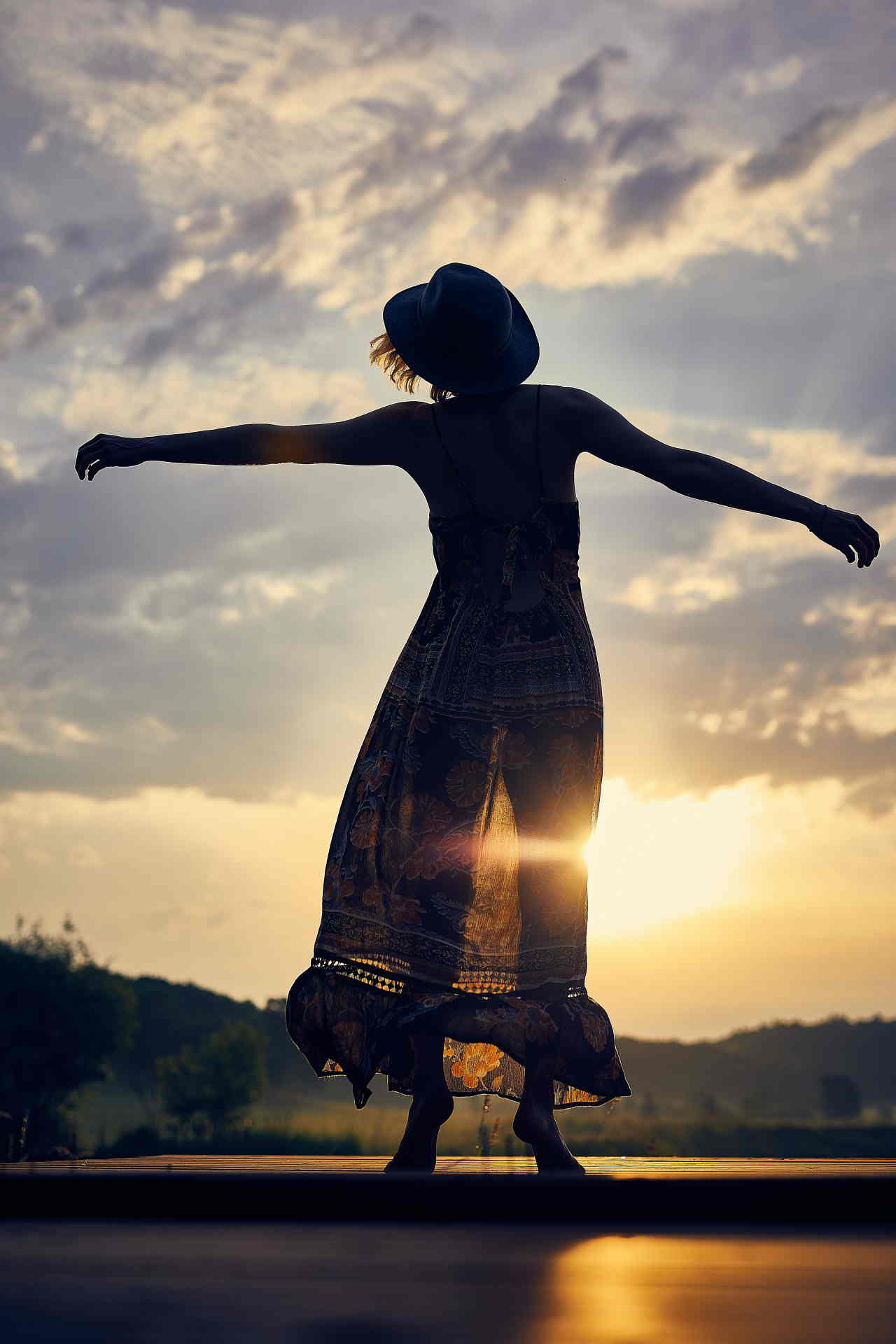 femme debout, de dos, les bras ouverts face au coucher de soleil