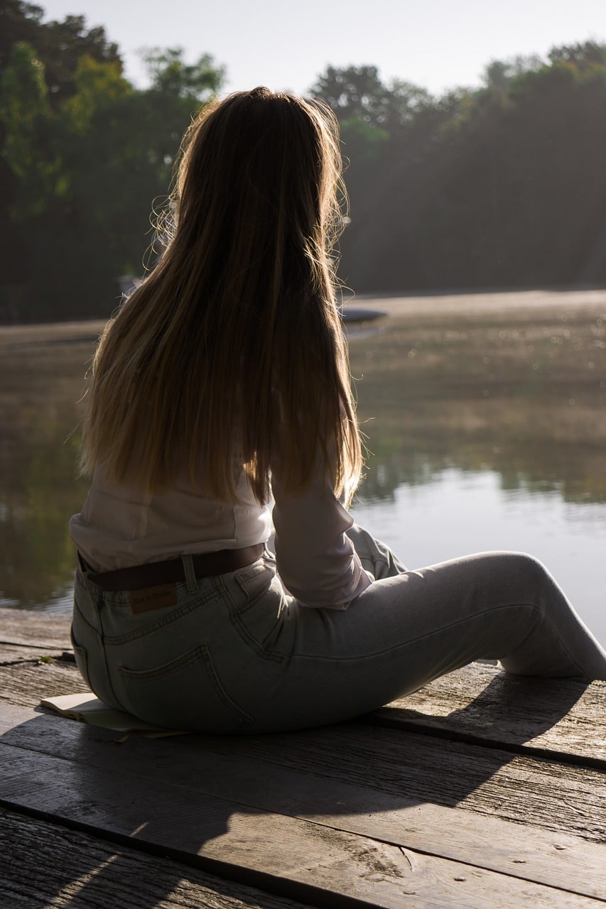 jeune femme assise sur le ponton d'un lac, pensive, qui regarde au loin