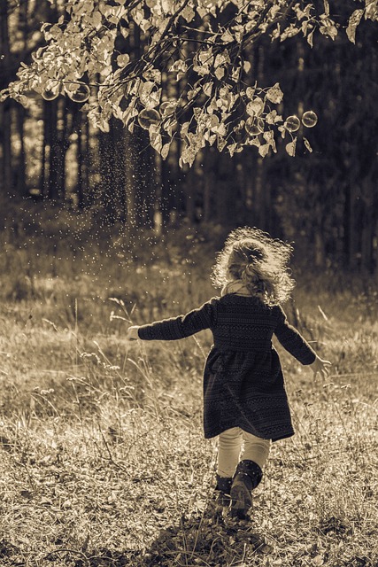 petite fille qui court dans l'herbe, de dos, à l'orée d'une forêt