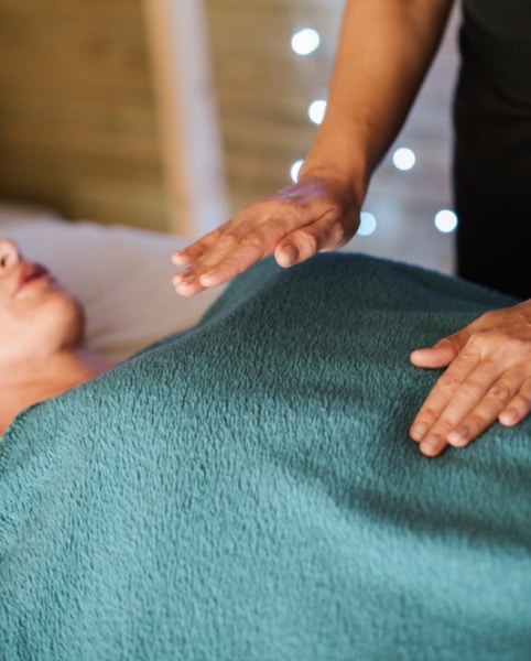 buste de femme allongée, recouvert d'une couverture verte, avec les mains d'une autre femme au-dessus d'elle